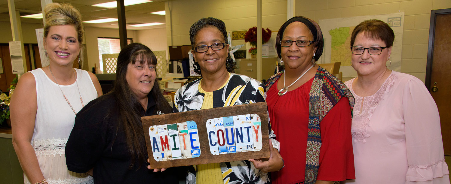 •	Five women standing and smiling inside an office