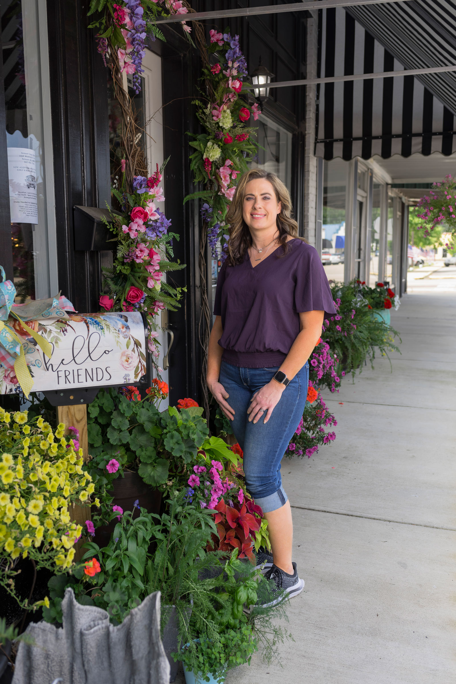 A woman standing outside beside flowers wreathing a door.