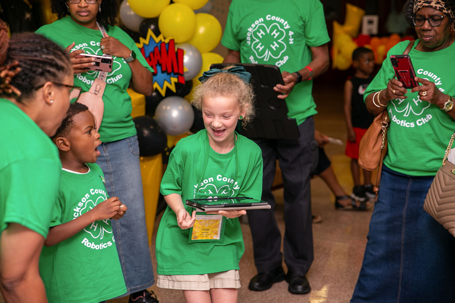 A little boy looks surprised at a girl grinning and holding an iPad.