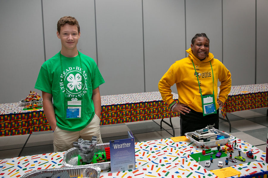 Two young men, one white and one black, with hands in their pockets, standing behind a table covered with LEGO.