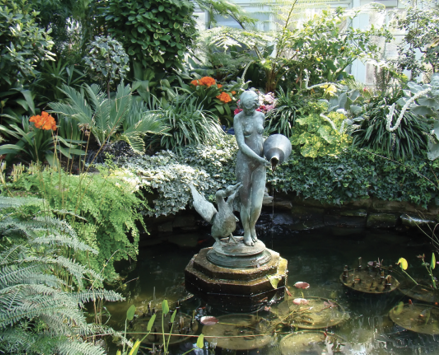 A garden pool with a statue in the center is lined with several green palms.