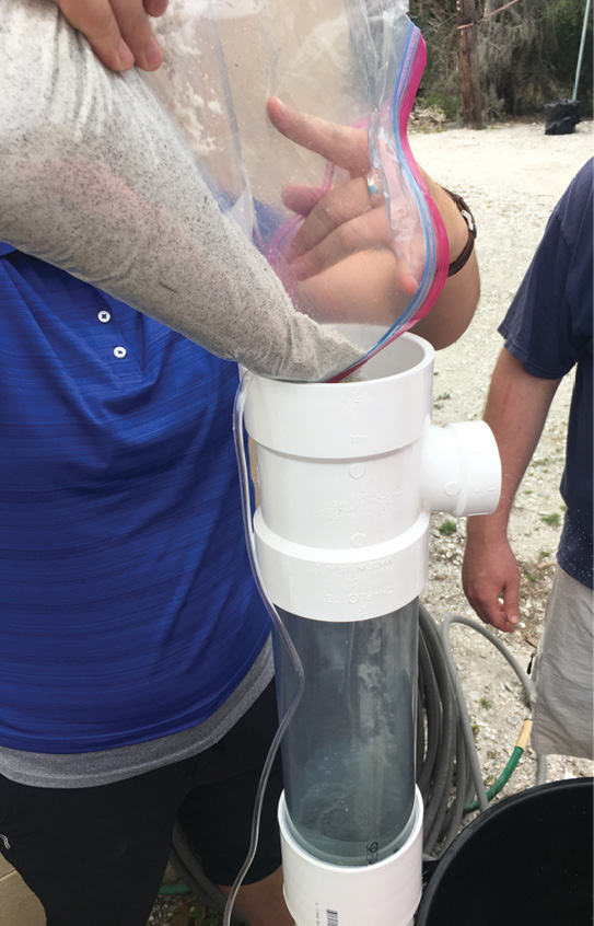 A person pours sand from a large plastic bag into a density separator.