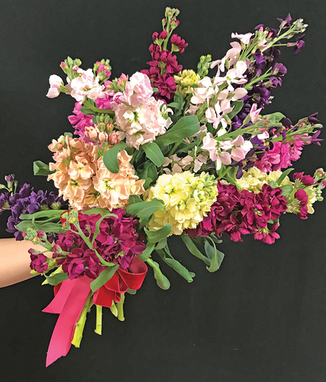 A person's arm cradling a very full, colorful bouquet of flowers.