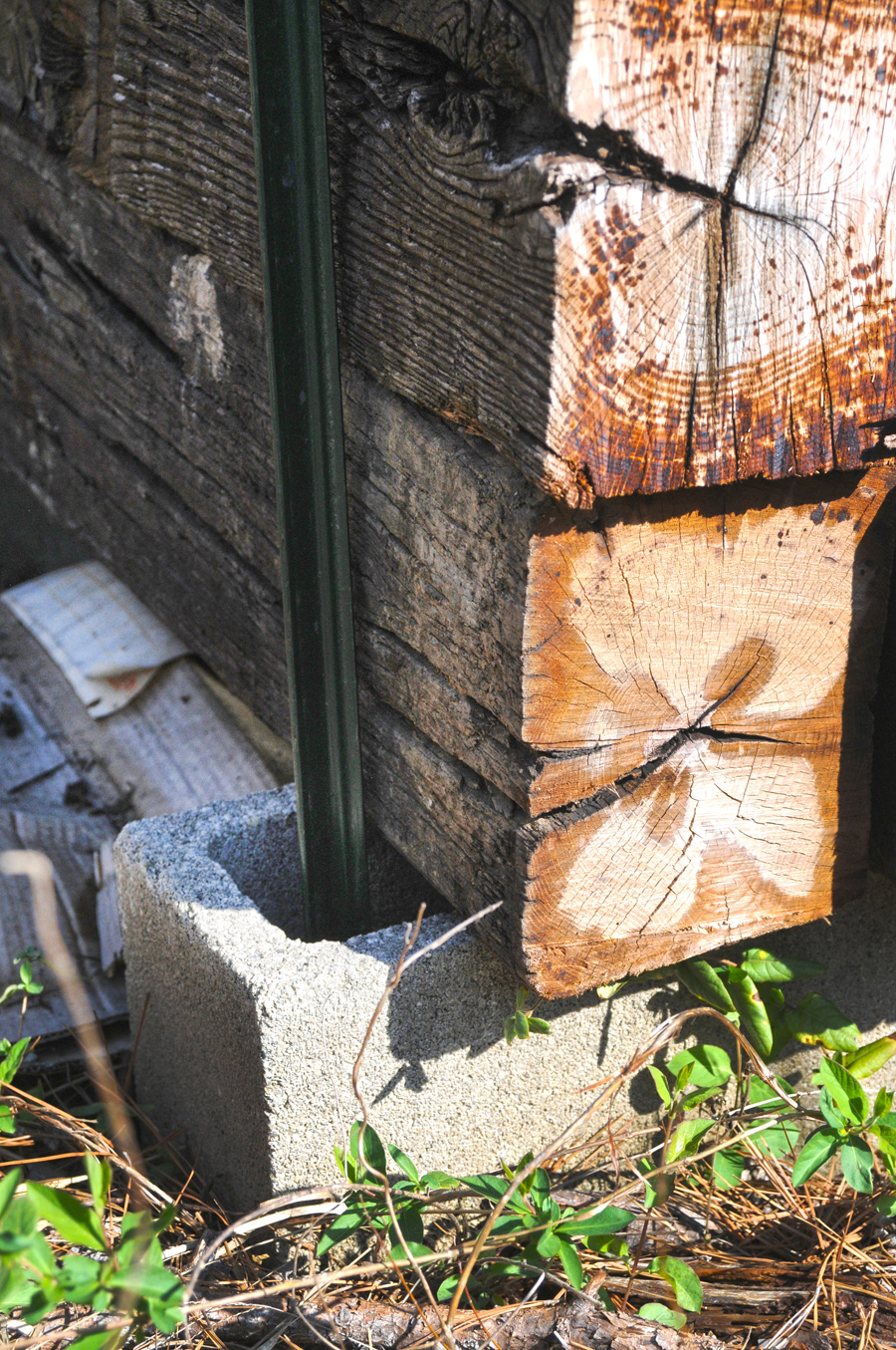 The reverse side close-up shows the T-post going through the hole of a cinder block. Two crossties are visibly flush against the T-post.