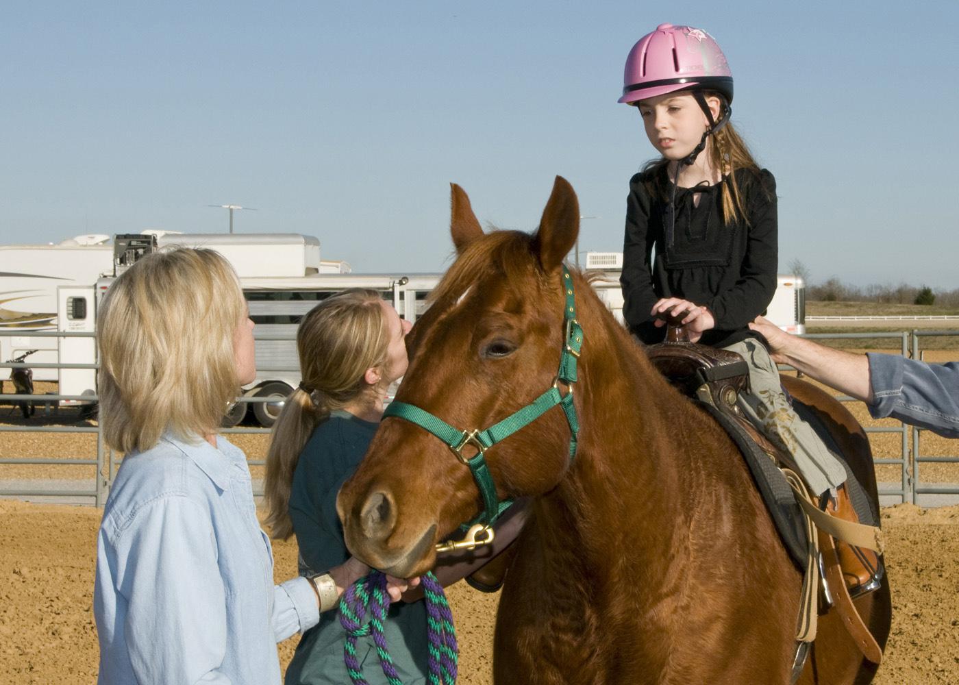 Mary Riley, coordinator for Mississippi State University's 4-H therapeutic riding program, and volunteer Shanna Holder, talk to 9-year-old Elizabeth Howard of Columbus as she sits atop her favorite horse, Bob. Howard's parents, Tommy and Brenda, are donating funds to construct a new therapeutic activity center in West Point. (Photo by Marco Nicovich)