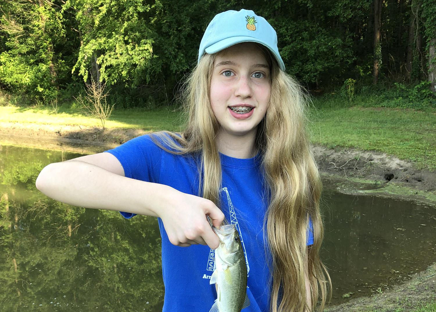 Girl in a blue T-shirt and baseball cap holding a small fish.