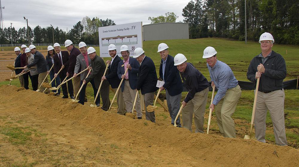 15 people with shovels and white helmets at groundbreaking.