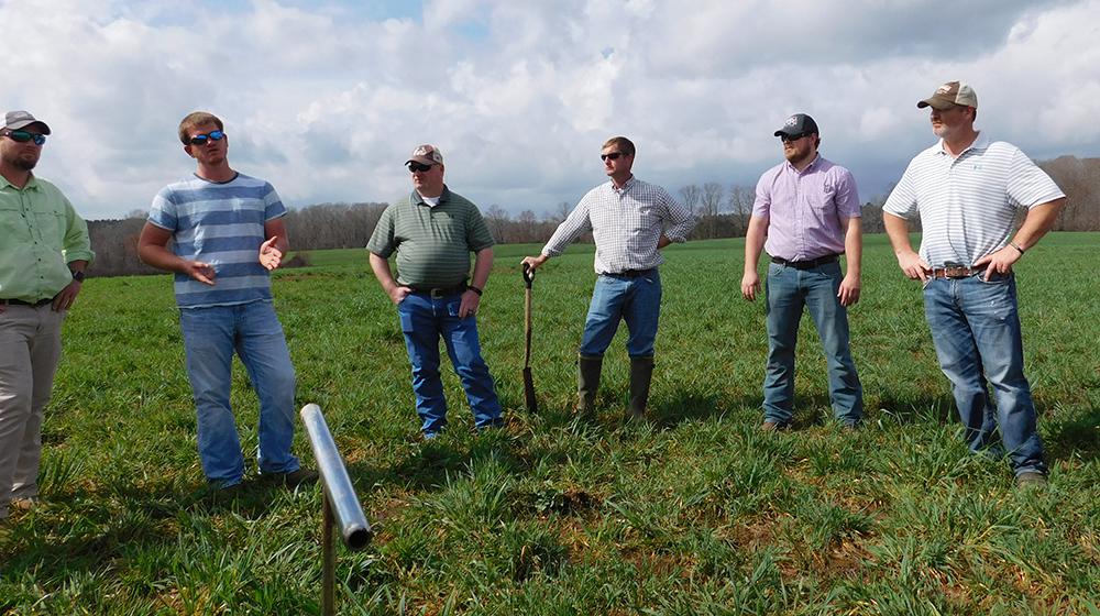 Man talking in grassy field while five other men listen.