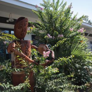 A piece of metal art shaped like a person standing in a flower and foliage arrangement.