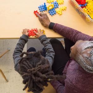 A boy building with shapes as a woman points to another piece.