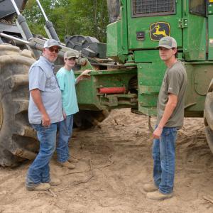 Three men standing in front of a piece of logging equipment.