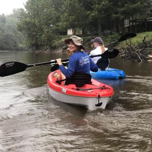 A smiling woman paddling a red kayak looks back at the camera.