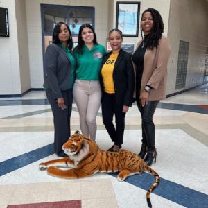 Four women standing smiling behind a plush tiger.