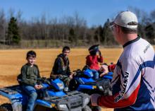 Three young people sit on ATVs as they listen to their instructor.