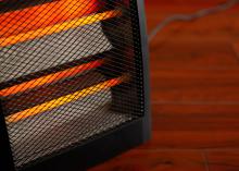 Close up of an electric space heater sitting on a hardwood floor.