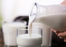 Hand pours milk from a glass bottle into a cup