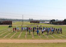 Dozens of people are scattered across a grassy field marked into squares.