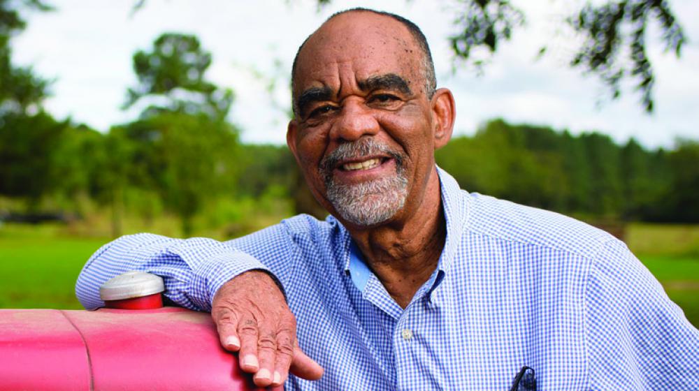 Smiling man in gingham dress shirt leans on a tractor