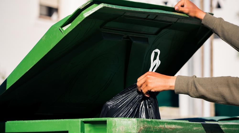 A person throwing a trash bag into a trash can.