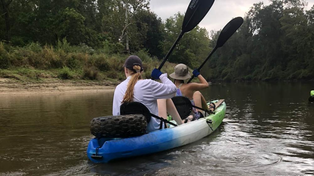 View from a green kayak of the back of two women paddling a kayak. 