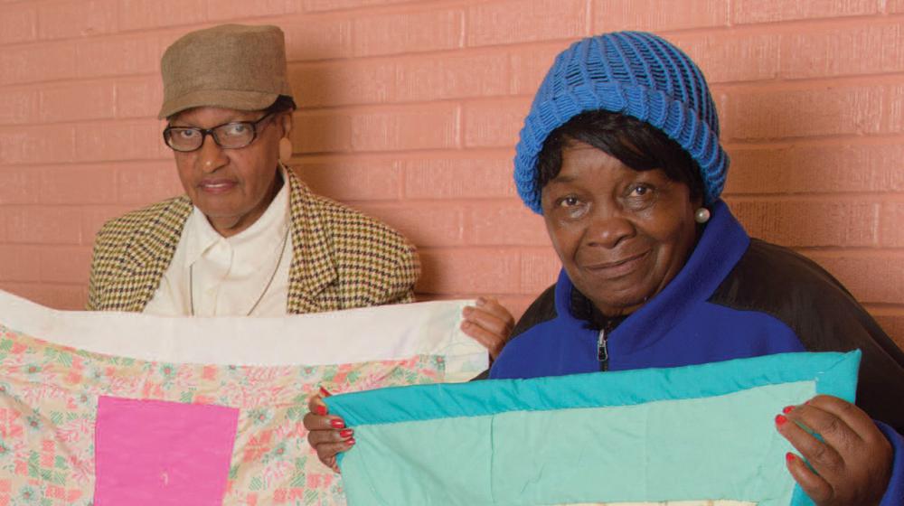 2 women hold up quilts.