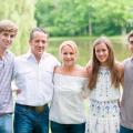 Family photo of 2 parents and 3 young adults standing with arms around each other in front of a small body of water.