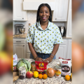 A woman in a kitchen with fruits and vegetables on the counter.