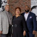 An older man and woman with a younger man stand smiling in front of a sign honoring Sadye Weir.