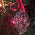 A small pink stocking with a white fuzzy top hangs from a Christmas tree inside a house.