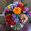 Orange, red, pink, purple, and yellow flowers are arranged in a glass bowl that sits atop a small, red table.