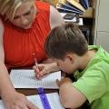 A woman looks on while a young boy writes on a piece of paper.