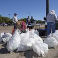 Person in straw hat tying up white trash bags.