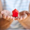 A small red toy house rests in a woman’s open hands.