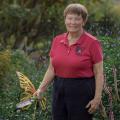 A woman holding a gardening tool stands in a green landscape.