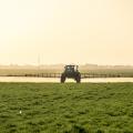 A tractor with a boom arm sprays crops.