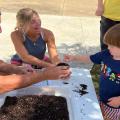 A man and a woman help a child plant seeds in a small pot of soil.