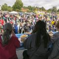 A large crowd gathers at a festival while a panel of judges tastes food.