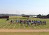 Dozens of people are scattered across a grassy field marked into squares.